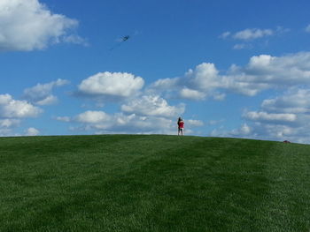 People walking on grassy field against cloudy sky