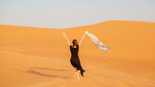 Woman with arms raised on desert against sky