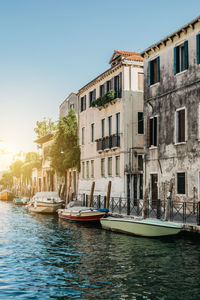 Boats moored on canal by buildings against clear sky