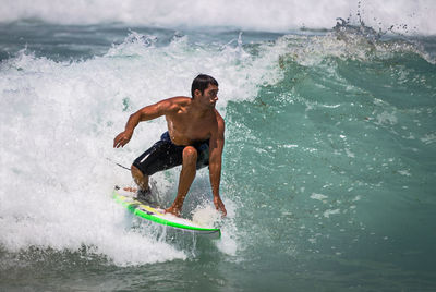 Full length of shirtless man splashing water in sea