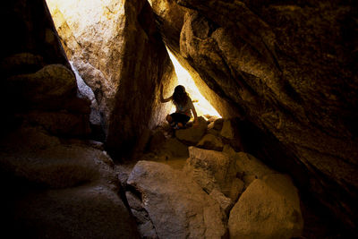 Young boy climbing under large boulders cave