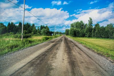 Empty road amidst field against cloudy sky