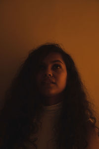 Close-up portrait of young woman against orange background