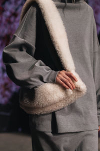Cropped figure of woman wearing the gray sport suit and white fluffy designer bag. fashion shot