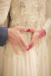 Midsection of bride with bridegroom making heart shape