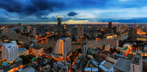 High angle view of city lit up against cloudy sky