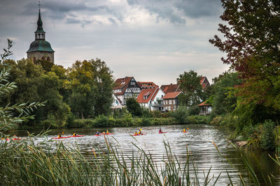 Lake amidst trees and buildings against sky