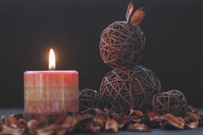 Close-up of lit candle by decoration and dry leaves on table