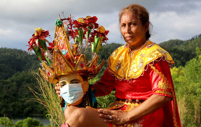 Portrait of woman standing by flowering plants against sky