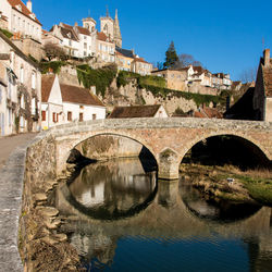 Arch bridge over river by old buildings against clear sky