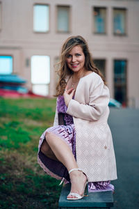 Portrait of smiling woman crouching on bench against building in city