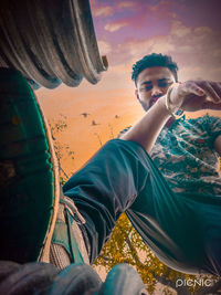 Full length portrait of young man sitting against sky