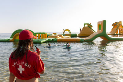 Lifeguard on rescue duty, standing on shore with whistle and looking to the aquapark. safety control