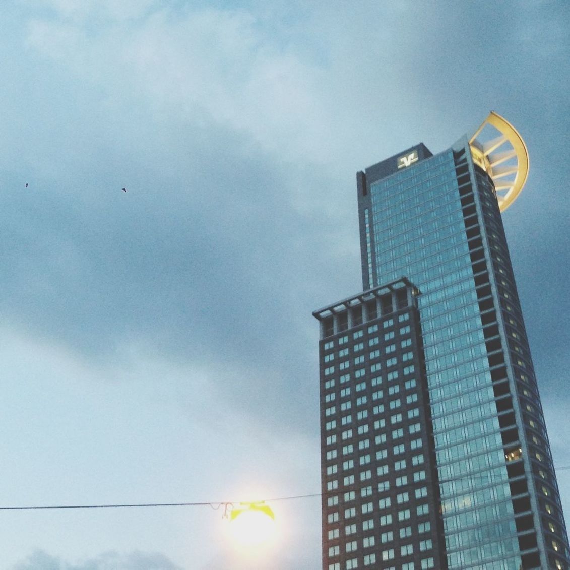 low angle view, sky, architecture, building exterior, built structure, cloud - sky, street light, cloud, cloudy, sunset, building, city, outdoors, no people, silhouette, sunlight, sun, modern, office building, lighting equipment