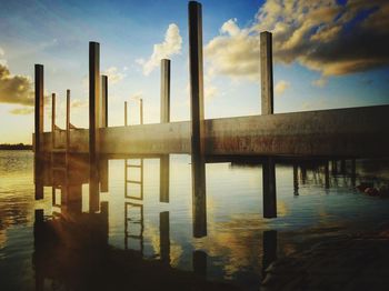 Pier on river against sky during sunset