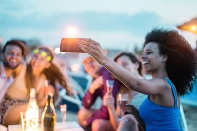 Smiling woman taking selfie with friends at dusk