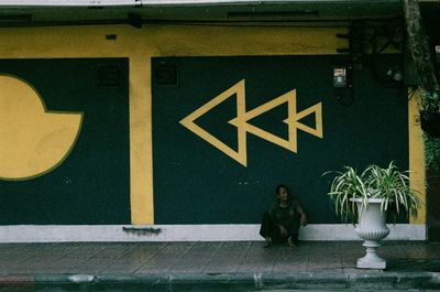 Man sitting on sidewalk against mural wall