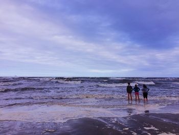 Rear view of men walking on beach against sky