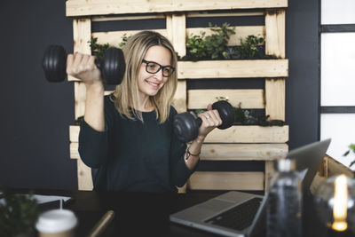 Smiling woman holding dumbbells at office