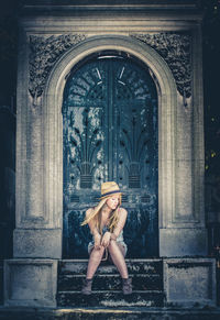 Full length of young woman sitting on steps against closed ornate door