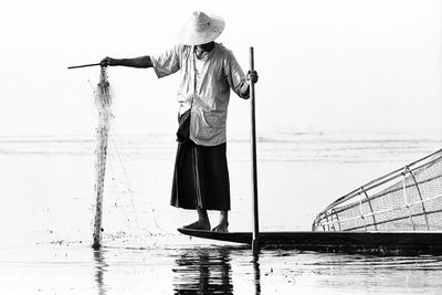 Full length of fisherman standing on boat in lake