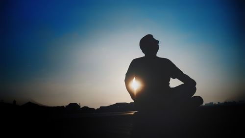 Silhouette man sitting against sky during sunset