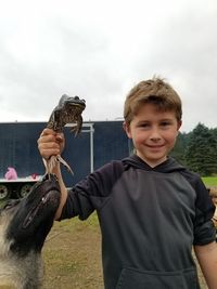 Portrait of smiling boy holding frog by dog on field 