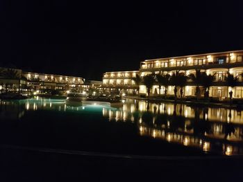 Illuminated buildings by river against sky at night