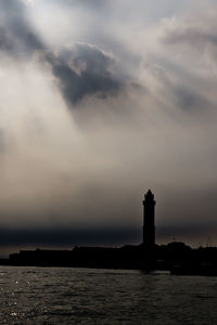 Silhouette built structure by sea against sky during sunset