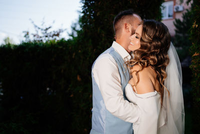 Newlywed couple embracing against trees