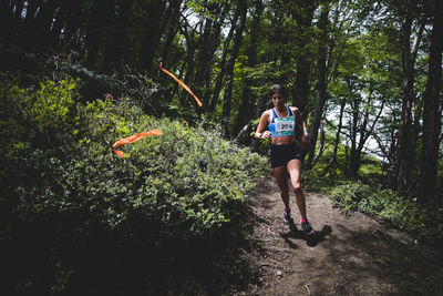 Full length of woman running on road amidst trees in forest