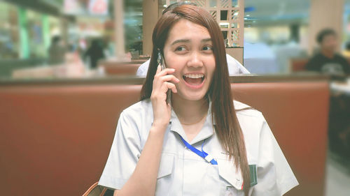 Smiling woman talking on mobile phone while sitting at restaurant