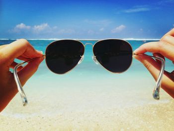 Close-up of hand holding sunglasses against sky