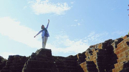 Woman with arms outstretched standing against sky