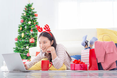 Young woman using mobile phone while sitting on christmas tree