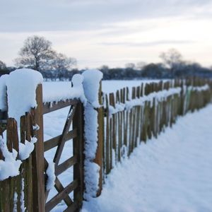 Wooden posts on snow covered landscape against sky