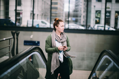Young woman looking down while standing on railing in city