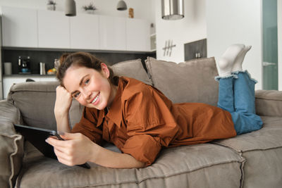 Portrait of young woman using mobile phone while sitting on sofa at home