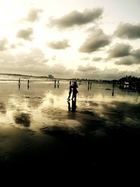 Silhouette people on beach against sky during sunset