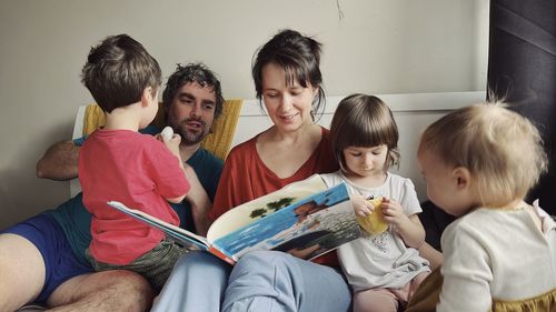 Happy parents reading a book to children sitting in the bed