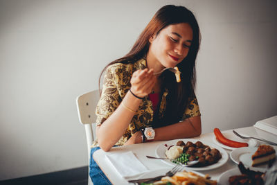 Portrait of a young woman sitting on table against wall