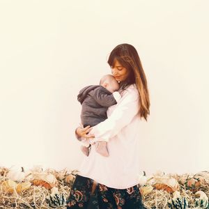 Mother holding baby on field against clear sky