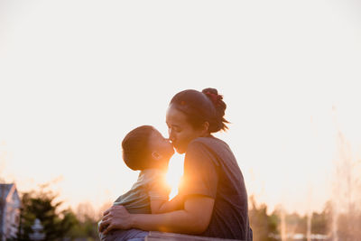 Mother and son kissing against sky during sunset