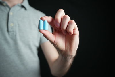 Midsection of woman holding pills against black background