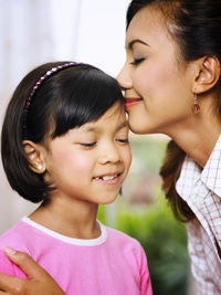 Smiling mid adult woman kissing daughter forehead