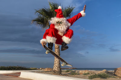 Mature man wearing santa claus costume skateboarding on footpath