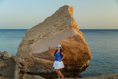 Woman standing on rock by sea against sky