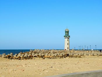 Lighthouse on beach by sea against clear blue sky