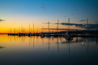 Sailboats moored at harbor against sky during sunset