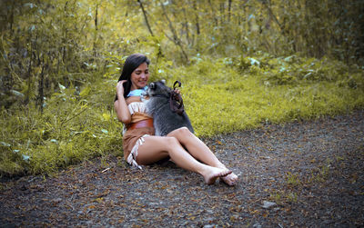 Young woman in traditional clothing playing with raccoon in forest